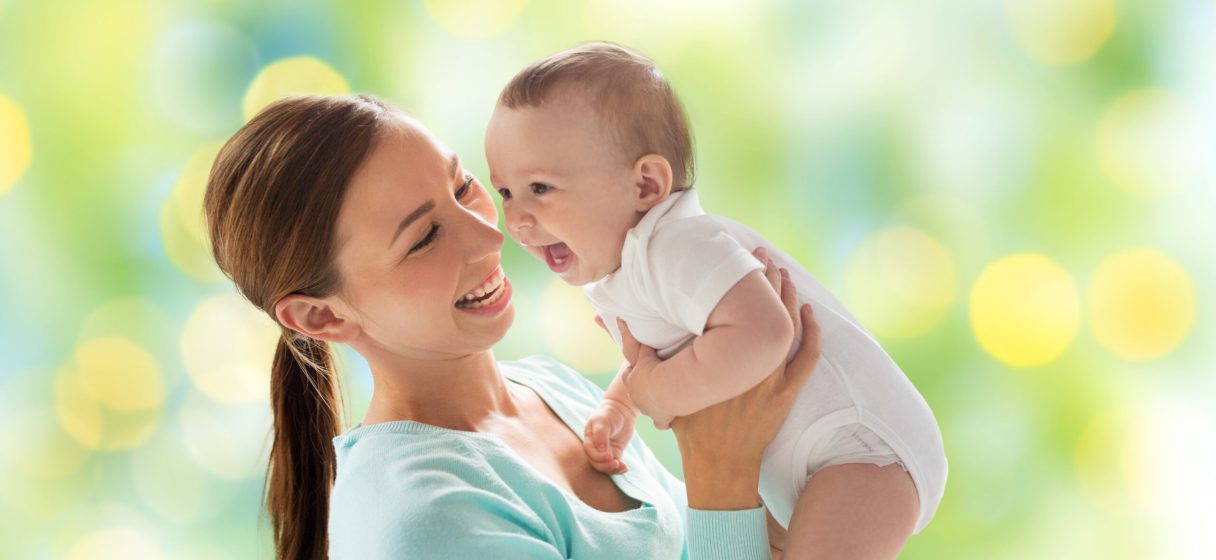 family, motherhood, child and parenthood concept - happy smiling young mother with little baby over green lights background