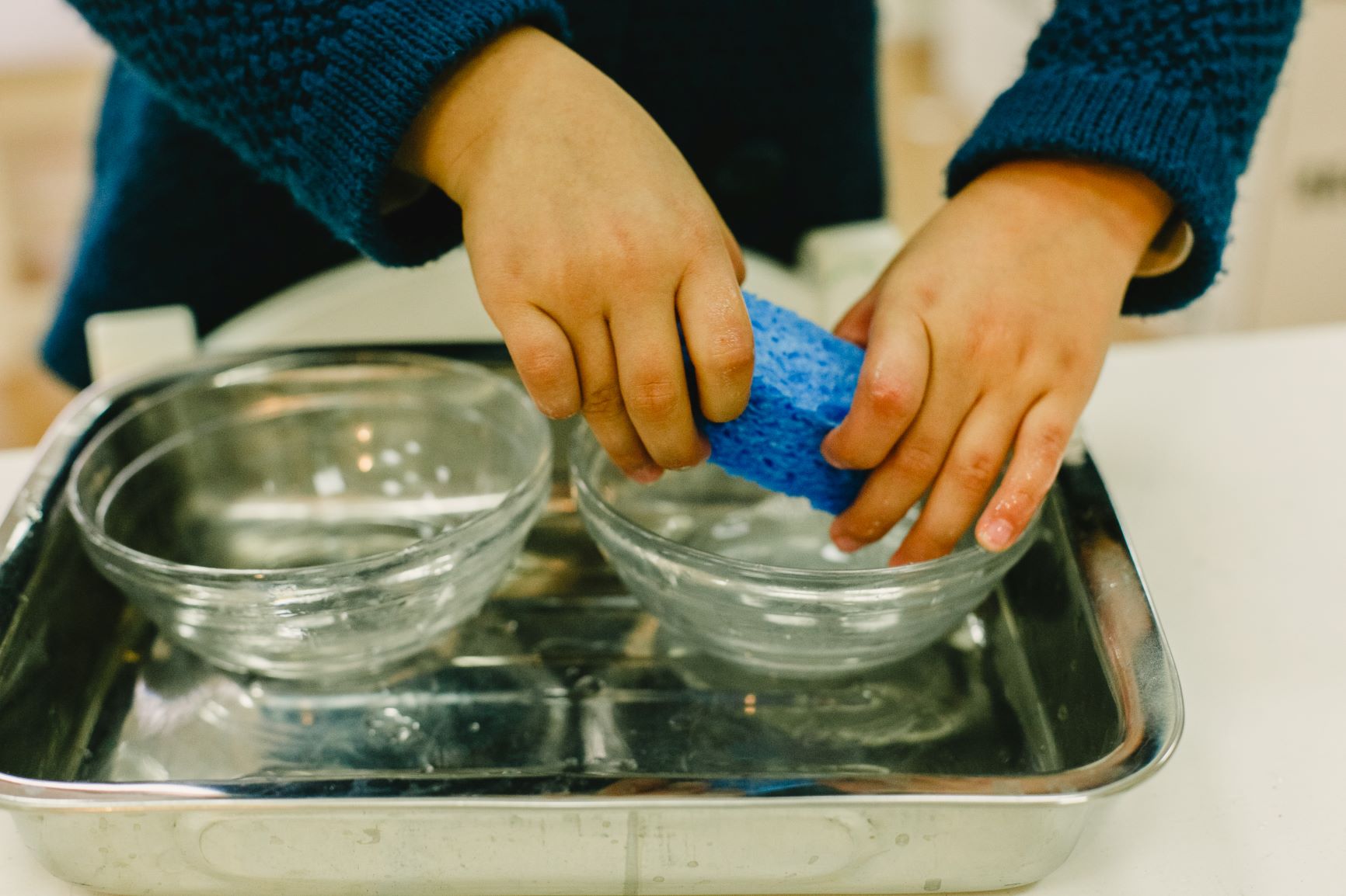 niño lavando los platos sin ayuda del asistente Montessori